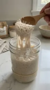 Homemade sourdough starter in a glass jar with fresh bread